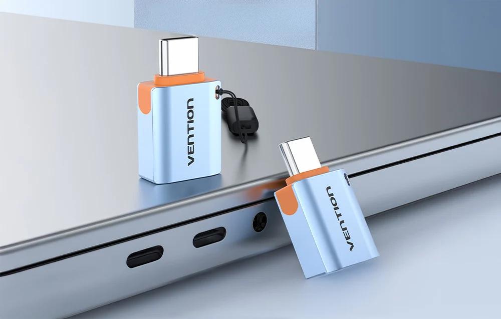 Två ljusblåa USB-A 3.1 till USB-C-adaptrar med rem, dator i bakgrunden