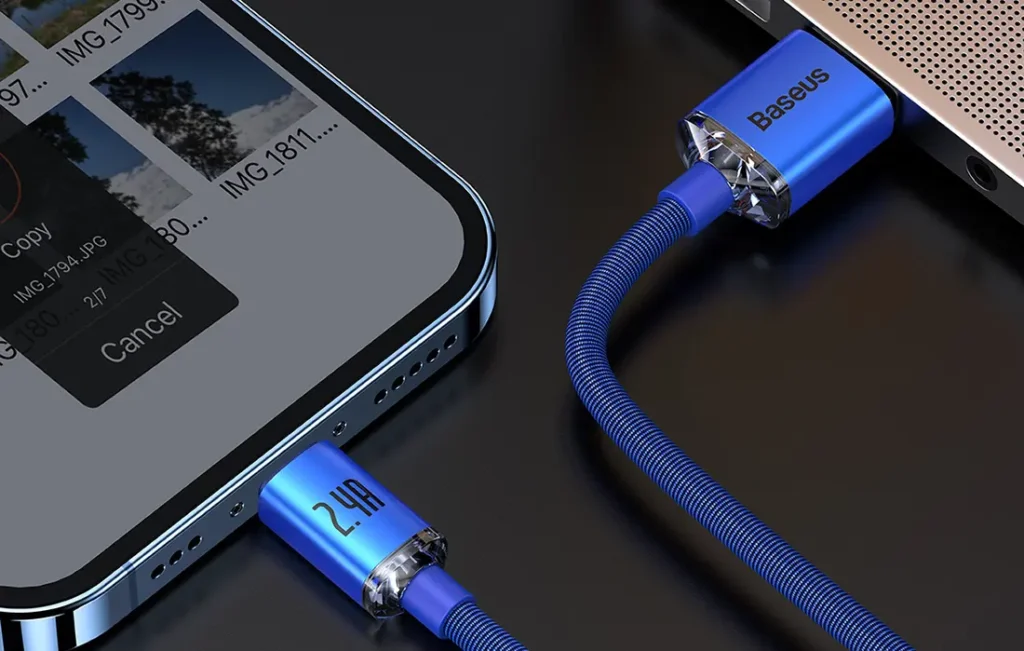 Blå USB-A till Lightning-kabel i tygmaterial med blå metallkontakter, iPhone ansluten till MacBook