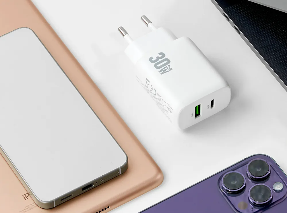 vit mobilladdare med text 30W, i bakgrunden mobiltelefoner och dator